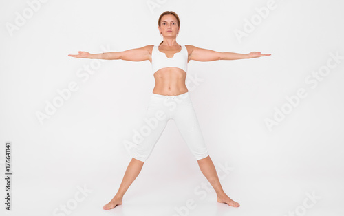 An adult woman doing yoga in a white hall.