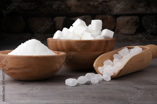 Bowl with white sand, crystal and lump sugar on wooden background.