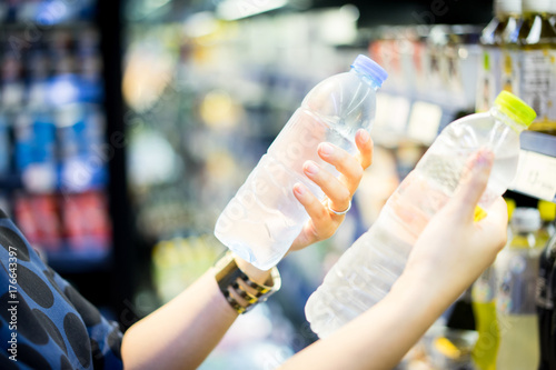 woman choosing cold bottle of water or beverage on shelves in supermarket store.