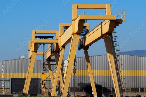 Wallpaper Mural Gantry cranes in front of a gray and yellow building of a manufacturing factory Torontodigital.ca