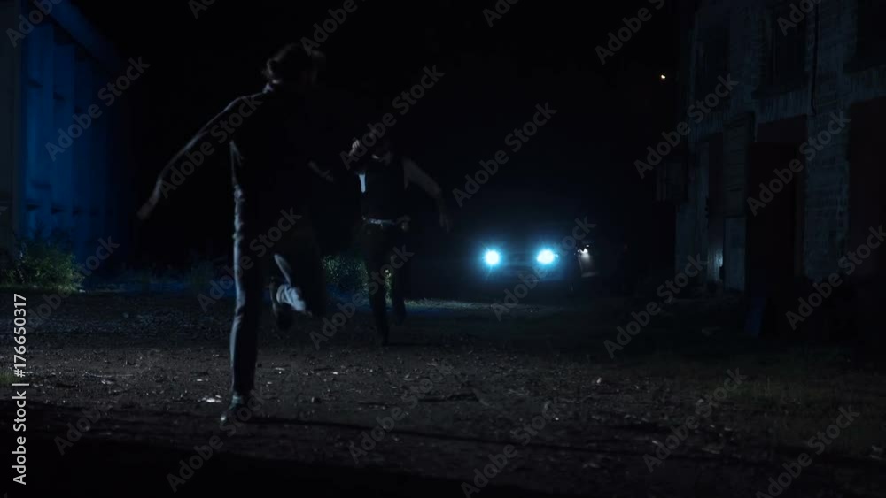 Brave police officer running after a dangerous suspect or wanted delinquent on a dark street in the suburbs at night