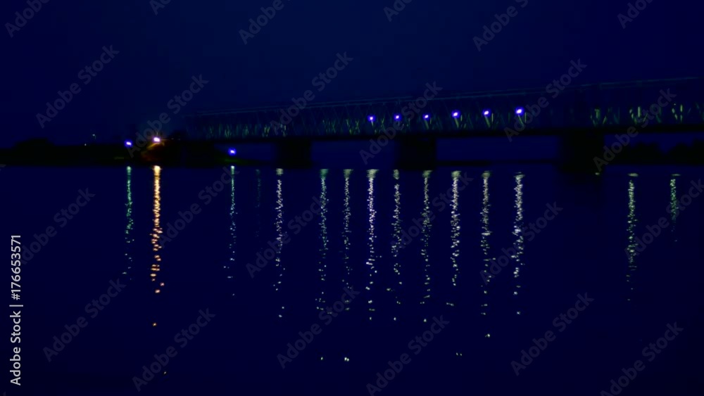 night, in the water the bridge and its lights are reflected. A long bridge over the river.