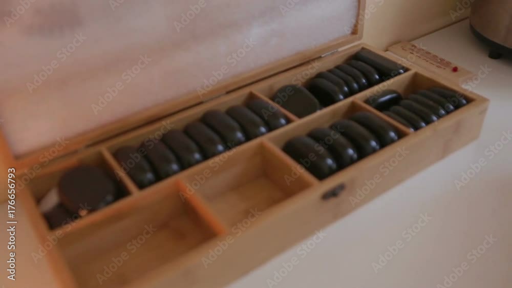 The massage therapist takes stones out of the box for massage and puts them into the heater The massage therapist takes stones out of the box for massage and puts them into the heater