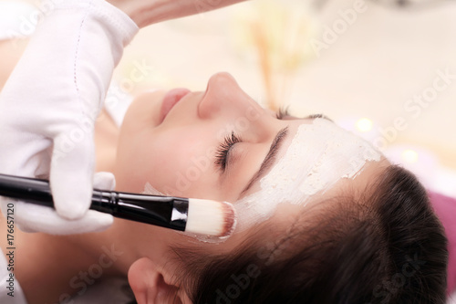 Young girl is enjoying facial procedure at beauty salon. She is lying and getting clay mask with pleasure