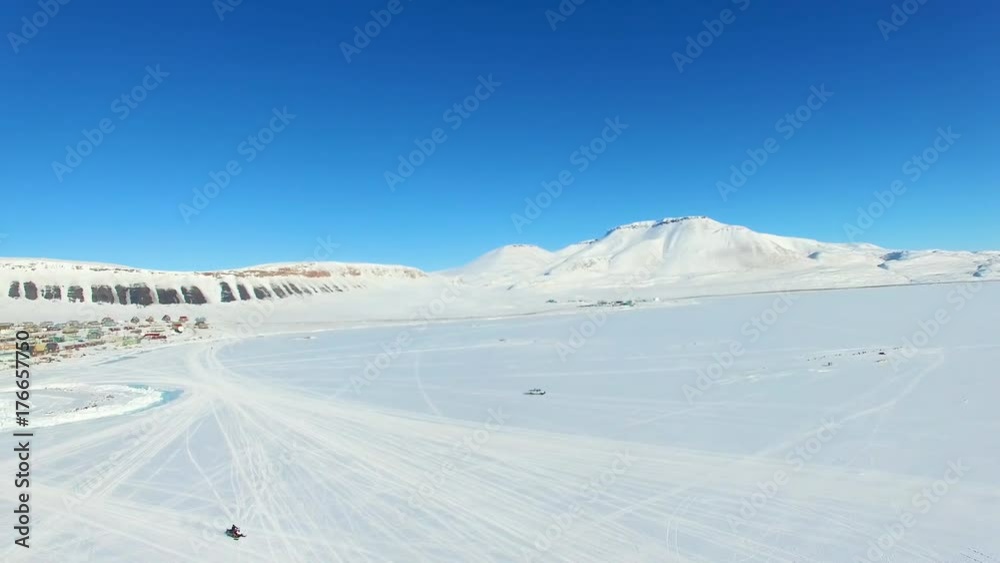 Aerial panning shot across a vast arctic landscape with a small town