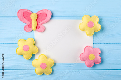Craft pink and yellow butterfly and flowers with white paper, copyspace on blue wooden background. Hand made felt toys. Abstract sky.