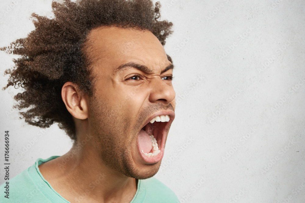 Half profile of aggressive male with dark curly hair, opens mouth ...