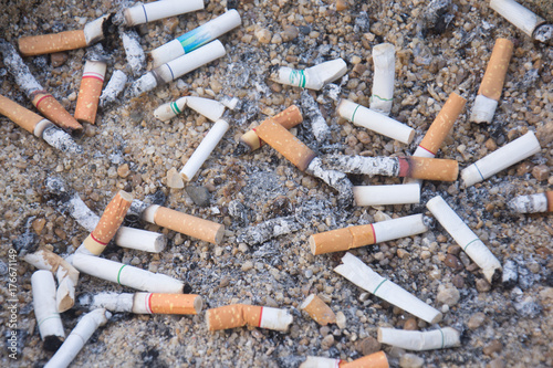 The rest of cigarettes in the ashtray. There are many types of cigarette stub on the sand in the ashtray.