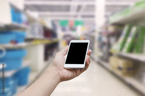 hand holding mobile smart phone with blank monitor screen on Supermarket blur background, business concept