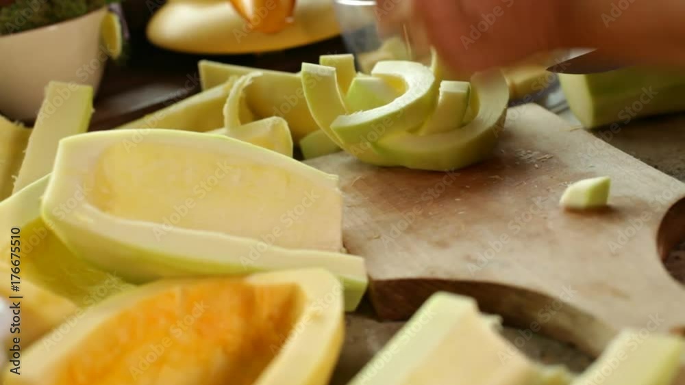 Hands chopping pumpkin slices on cutting board, putting the pieces in bowl - sliding camera Hands chopping pumpkin slices on cutting board, putting the pieces in bowl - sliding camera