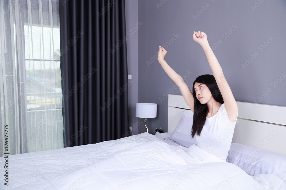 Woman waking up and hand raised on bed in bedroom