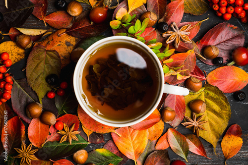 Cup of tea with autumn leaves, nuts, berries and spices on the rustic background. Shallow depth of field.