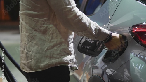 Young man fueling his car at gas station, using the pump nozzle. Late at night © starsstudio