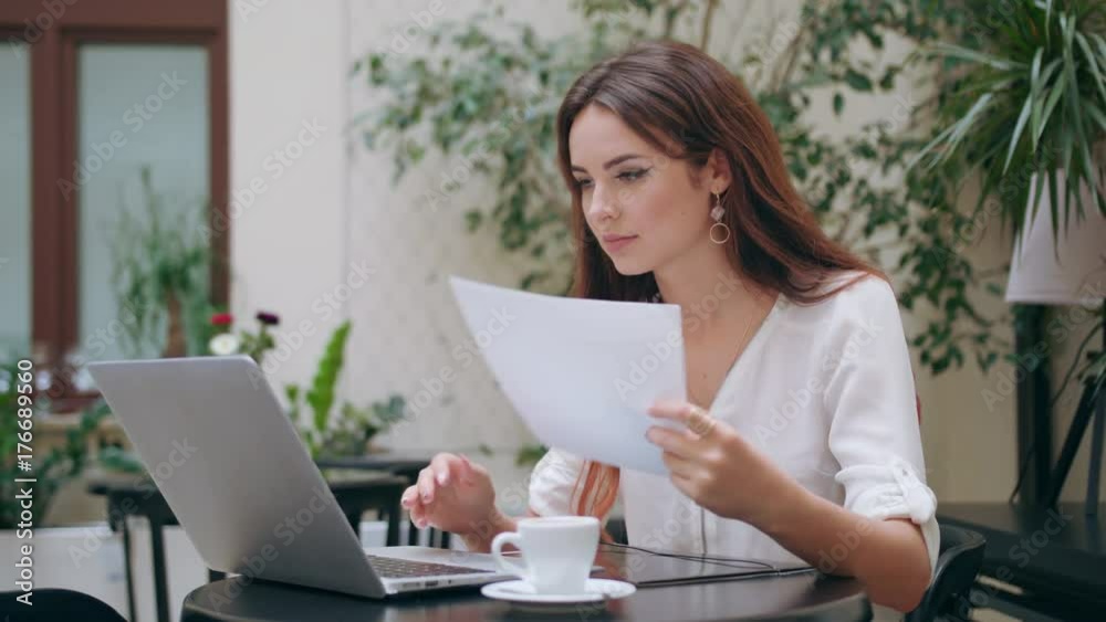 A beautiful girl using her laptop and verifying data with a sheet of paper in the room. Medium shot. Soft focus. A beautiful girl using her laptop and verifying data with a sheet of paper in the room. Medium shot. Soft focus.