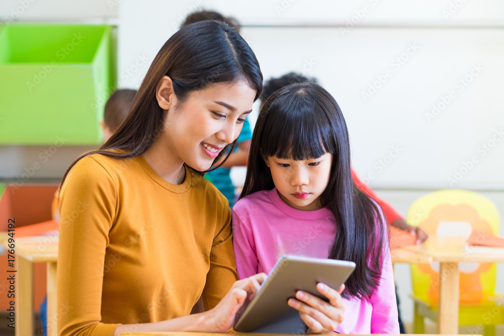Asia woman teacher teach girl student with tablet computer in classroom at kindergarten preschool,Online education concept. Asia woman teacher teach girl student with tablet computer in classroom at kindergarten preschool,Online education concept.