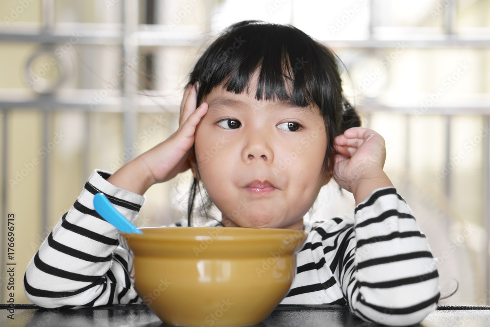 Asian children cute or kid girl student anorexia or sad and holding food in mouth with vacant and prop up or hand to cheek on food table for breakfast before going to school for study Asian children cute or kid girl student anorexia or sad and holding food in mouth with vacant and prop up or hand to cheek on food table for breakfast before going to school for study