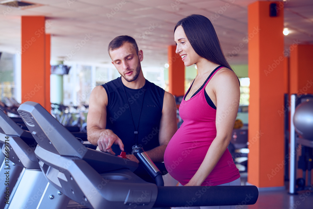Pregnant woman exercising on treadmill with personal trainer Pregnant woman exercising on treadmill with personal trainer