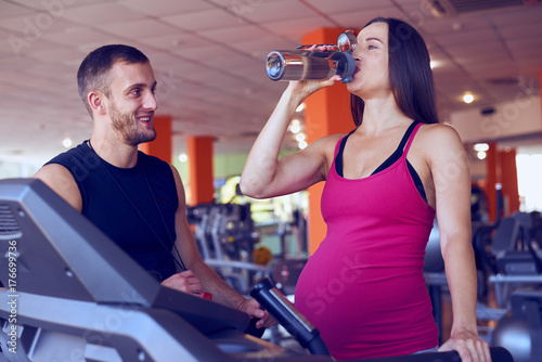 Pregnant woman drinking water while running on treadmill