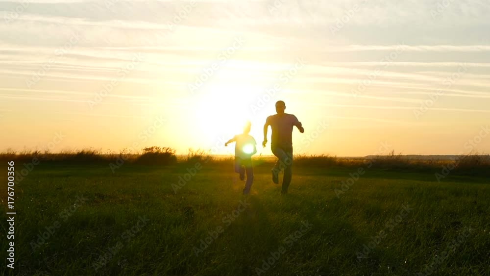 Happy family father and son running across the green field against the sunset background Happy family father and son running across the green field against the sunset background