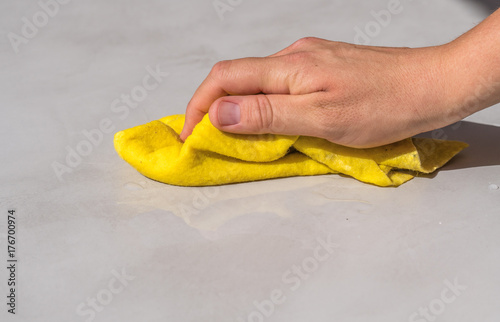 woman's hand cleaning spilled water on a cement floor with a yellow floor cloth dishcloth closeup