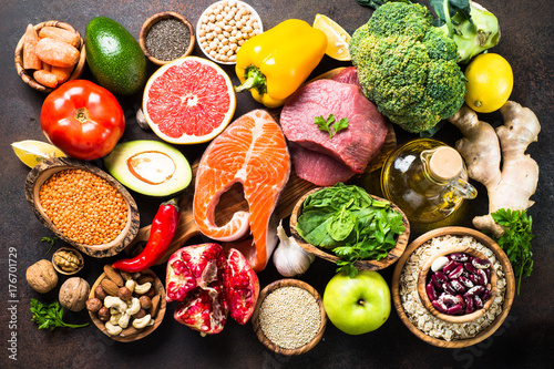 Balanced diet food background. Organic food for healthy nutrition, superfoods. Meat, fish, legumes, nuts, seeds, greens, oil and vegetables. Top view on dark stone table.