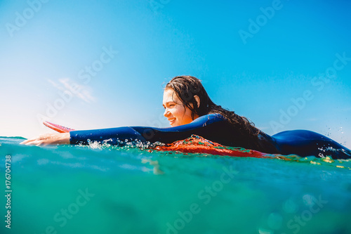 Surf girl is smiling and rowing on the surfboard. Woman with surfboard in ocean during surfing. Surfer and ocean