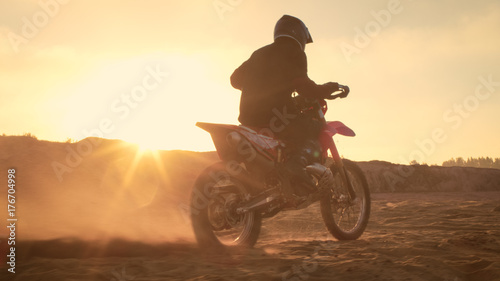 Professional FMX Motorcycle Rider Twists Full Throttle Handle and Starts Riding on the Sandy Off-Road Track. Scenic Sunset. © Gorodenkoff