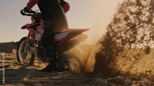 Back View Footage of the Professional Rider on the FMX Dirt Bike Twisting Full Throttle Handle and Digging into the Sand with His Back Wheel.