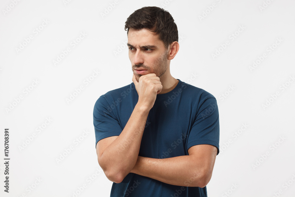 Skeptical and dissatisfied young man in blue t-shirt touch his chin with hand. Doubt concept Skeptical and dissatisfied young man in blue t-shirt touch his chin with hand. Doubt concept