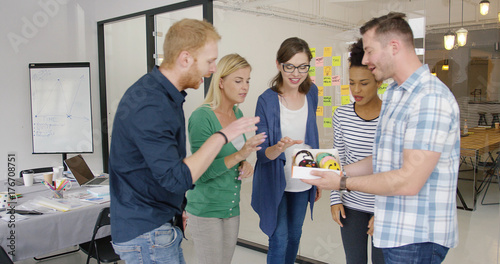 Εκτύπωση καμβά Side view of young man holding box with doughnuts and treating delighted coworkers gathering in modern office