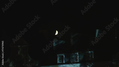 Half moon shining in the sky over the house roof at night. Medium shot photo