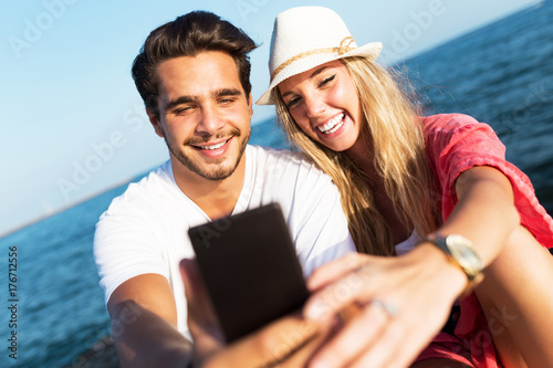 Beautiful young couple using mobile phone on the beach.