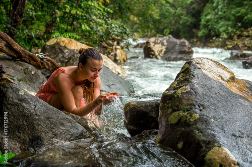 the girl drinks water from a mountain stream