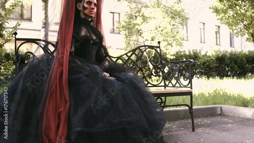 Halloween girl in witch sitting on a bench in the city park forest. Mystery and horror concept. photo