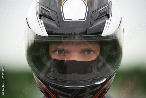 Close up shot of blue eyed Caucasian male wearing stylish motorcycle helmet, staring at camera with confident determined look before race. People, extreme sports, active lifestyle, speed and adrenalin