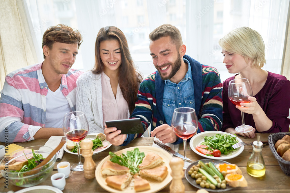 Portrait of four happy people smiling happily while watching video from smartphone at dinner table during holiday celebration Portrait of four happy people smiling happily while watching video from smartphone at dinner table during holiday celebration