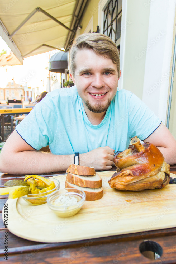 Young man eating smoked pork leg meat and drinking beer