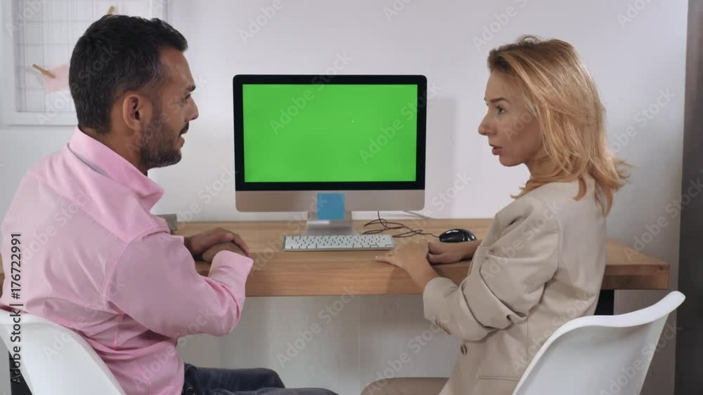 Business negotiation in office. Handsome professional man giving presentation showing on computer with green display. Caucasian blonde adult woman looking on screen pc listens attentively and showing