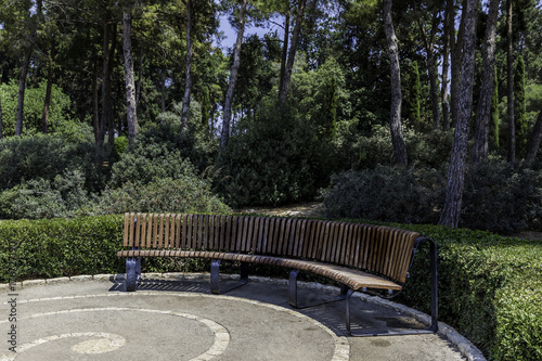 Half round curved crescent shaped bench in the park with trees and bushes in background