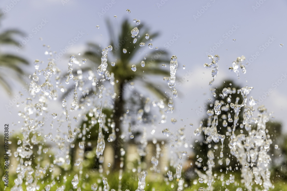 Fountain bubbling up water jets and drops frozen in the midair on green nature with palm trees background