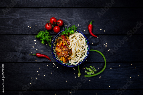 Traditional asian noodle lagman with vegetables and meat. Top view dark wooden background photo