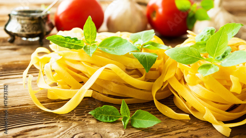 Raw tagliatelle pasta with fresh basil, garlic and tomatoes on rustic wooden table