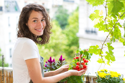 Young woman taking care of her plants and vegetables on her city balcony garden - Environment and ecology theme