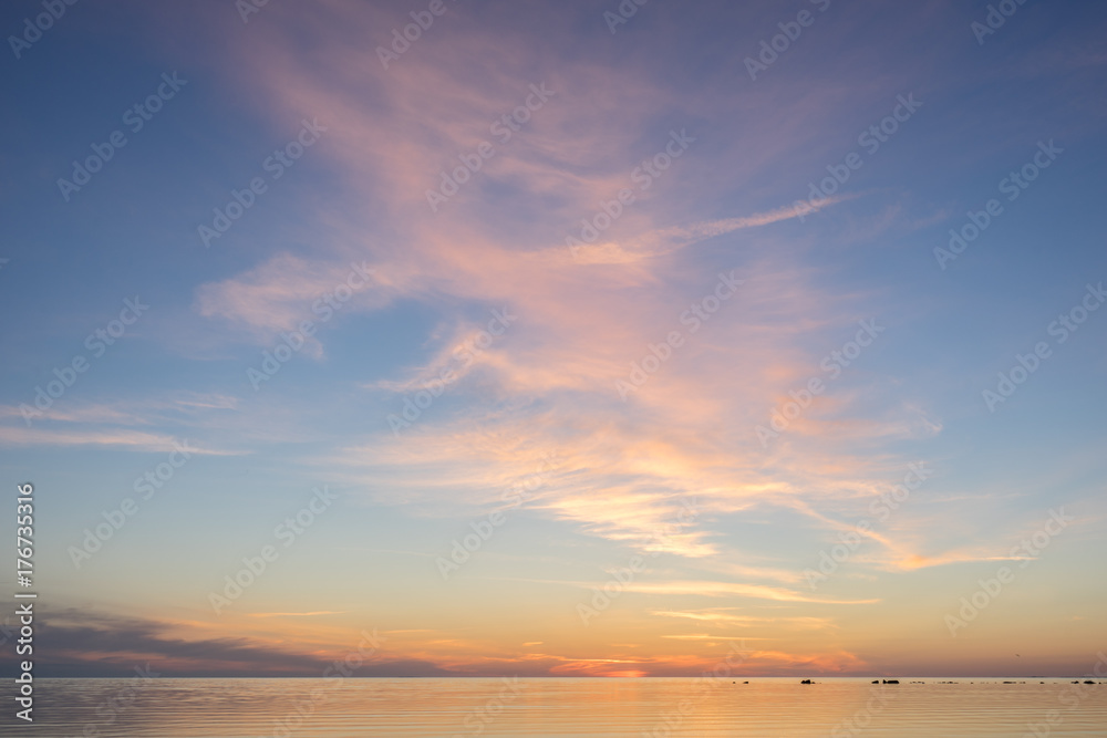 Fototapeta premium Evening sunlight on coast, pink clouds, blue sky reflection on water. Beach in summer. Seaside natural environment. Shore in Kesselaid, small island in Estonia. Nature Reserve in North Europe