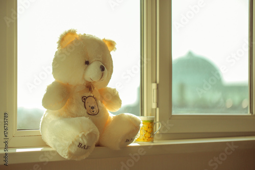 yellow, soft toy bear sits at the window under daylight and tea mug