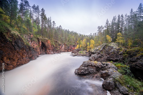 Red cliff, stone wall, forest, waterfall and wild river view in autumn. Fall colors - ruska time in Kiutaköngäs. One part of Karhunkierros Trail. Oulanka National Park, north Finland, Lapland, Europe