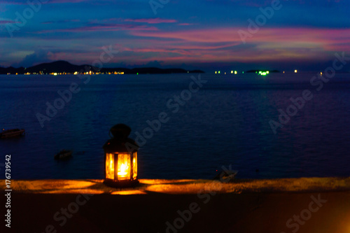 The light or lantern is shining in the dark and placed on the edge of the mortar with sea and twilight sky at night as background.