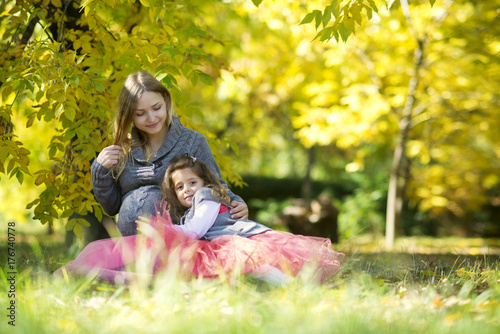 Pregnant mother with her daughter lies in the autumn park