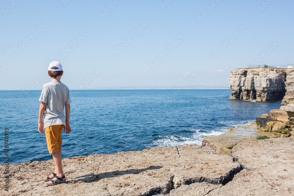The boy is standing on the rocks