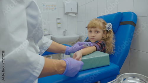 Nurse is taking blood sample from a vein in the arm of little girl